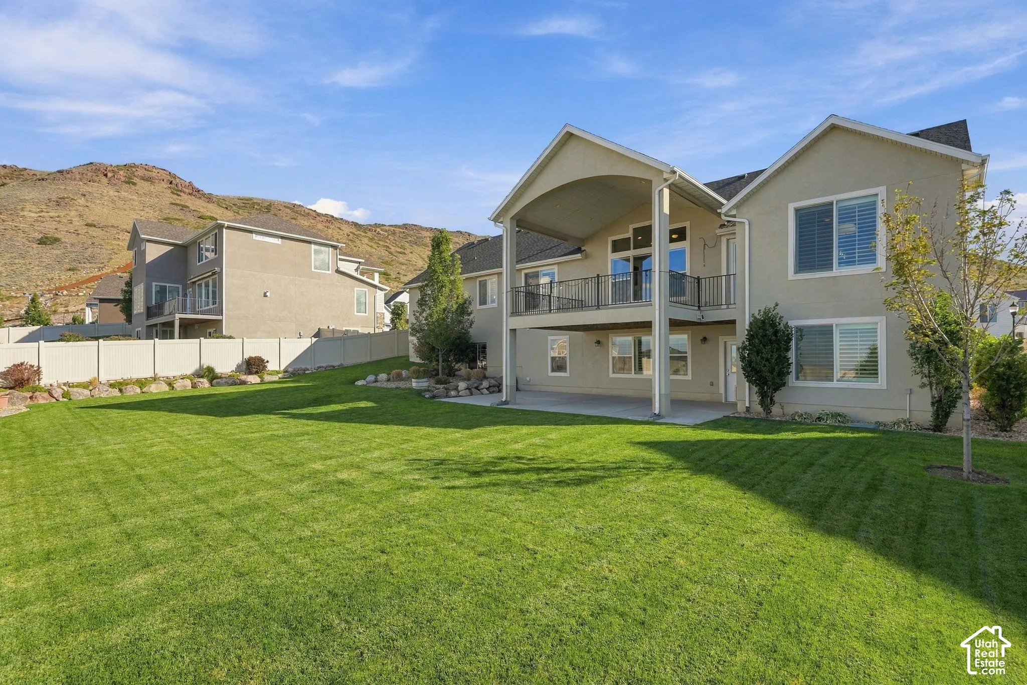 Expansive landscaped backyard with a manicured lawn, a covered upper-level deck with black railings, and a lower-level covered patio