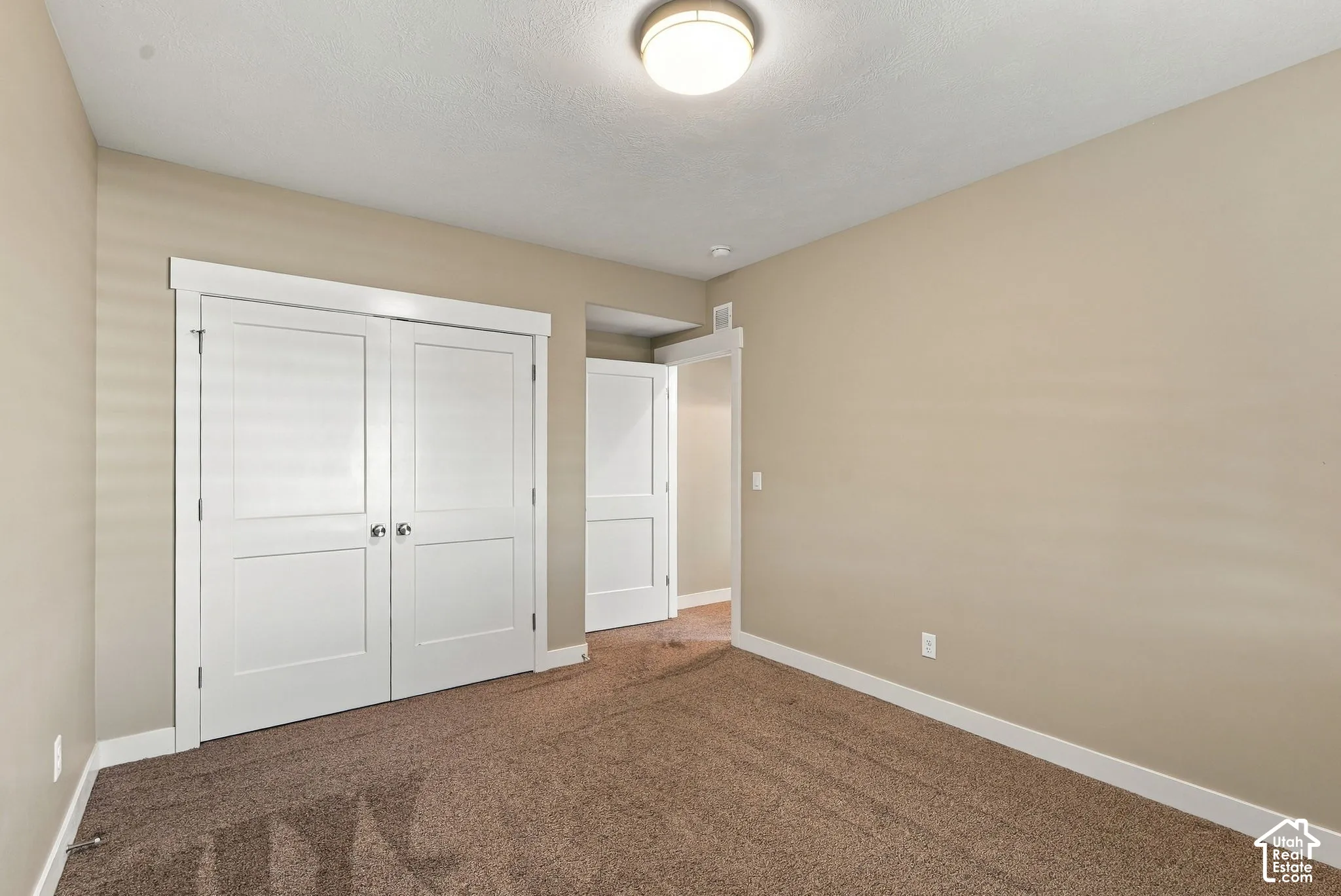 Basement three, neutral wall color, plush carpet, white trim, overhead flush-mount lighting, and bi-fold closet doors