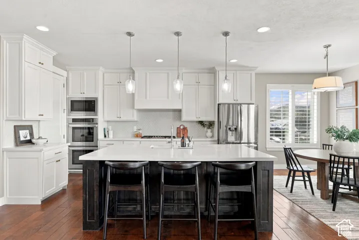Kitchen featuring a large island with seating, white shaker cabinetry, stainless steel appliances, and wood-finish flooring