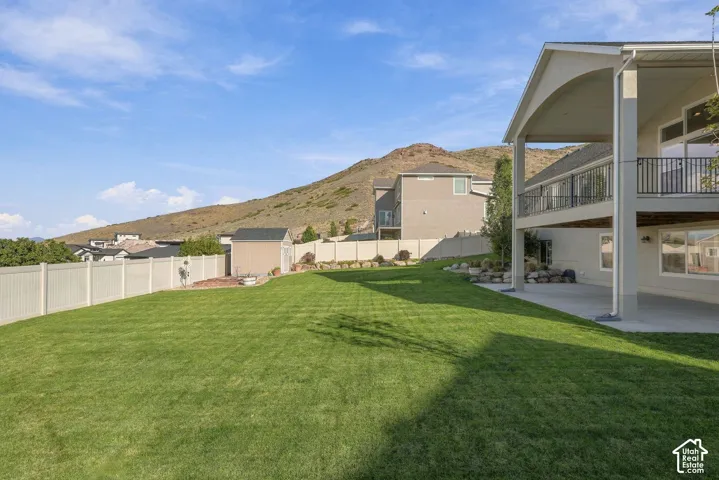 Expansive lawn with a white privacy fence, storage shed, and paved patio