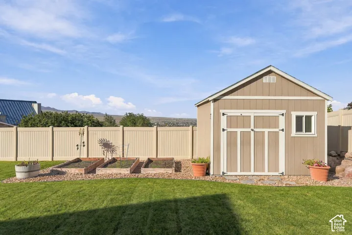 Detached shed with gable roof, vinyl fencing, raised garden beds, and manicured lawn