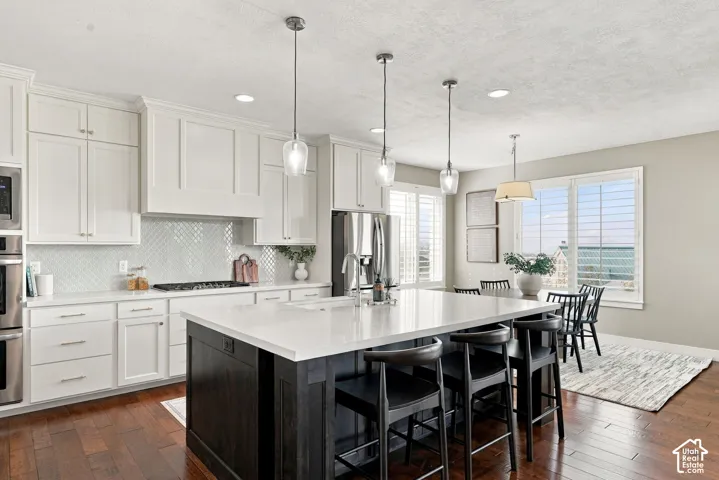 White shaker cabinetry, dark wood-finish flooring, white countertops, stainless steel appliances, and a tiled backsplash