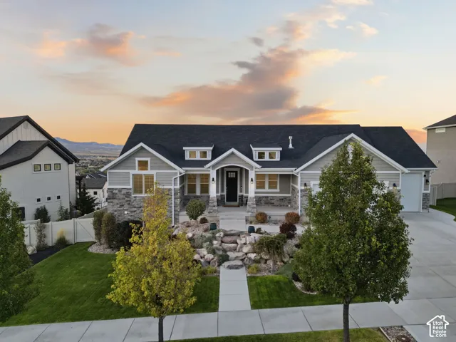 Front exterior featuring stone and siding finishes, a dark shingle roof, an attached garage, a concrete driveway, and a landscaped front yard with mature trees