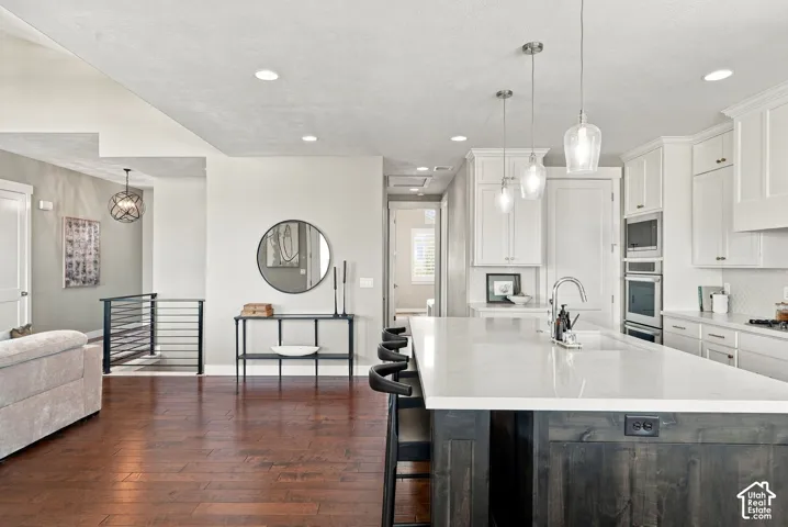 Open-concept kitchen featuring an oversized island with seating, pendant lighting, white cabinetry, and stainless steel built-in appliances
