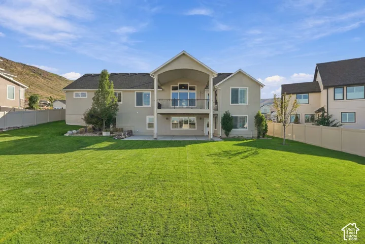 Expansive backyard featuring a manicured lawn, an upper-level balcony with a black railing, and a lower-level covered patio