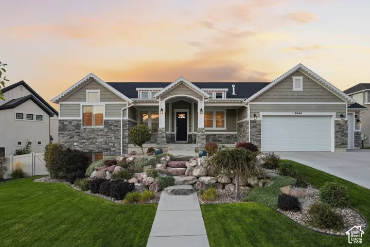 Stone and siding exterior with dark trim accents, concrete driveway, and a three-car garage