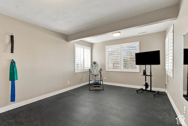 Basement bedroom four, workout room, recessed ceiling lighting, two windows with white plantation shutters, durable rubber flooring, and a wall-mounted mirror