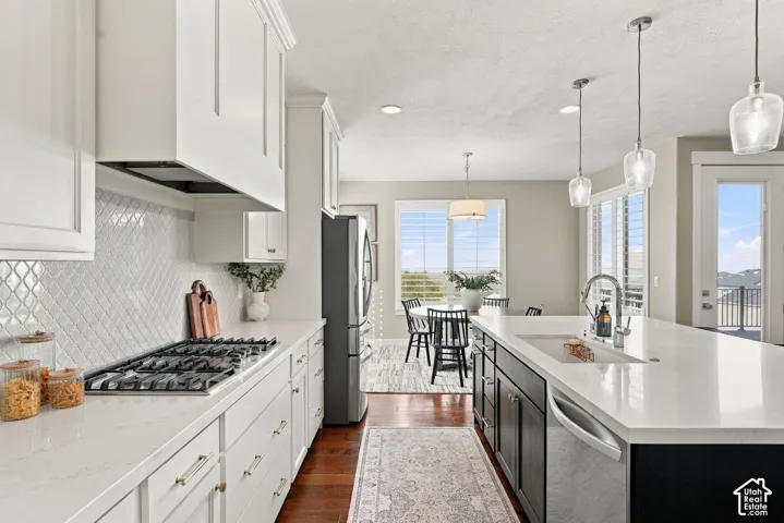White shaker cabinetry, gas cooktop, tile backsplash, stainless steel appliances, and a kitchen island with an undermount sink