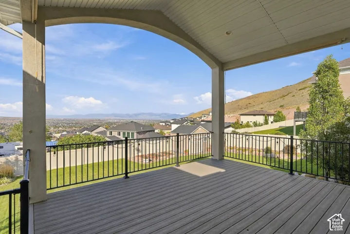 Expansive covered deck featuring composite decking, an arched concrete support, and black metal railings overlooking a landscaped yard and distant terrain