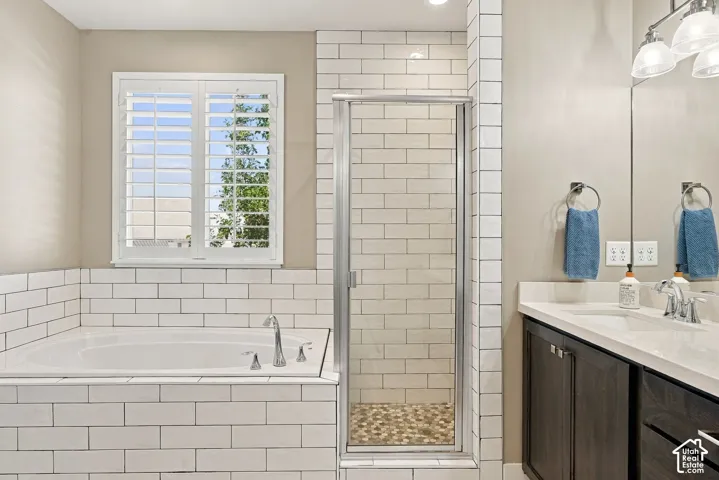 Corner soaking tub with subway tile surround, separate glass-enclosed shower with subway tile walls and pebble floor, single vanity with integrated sink, and white window shutters