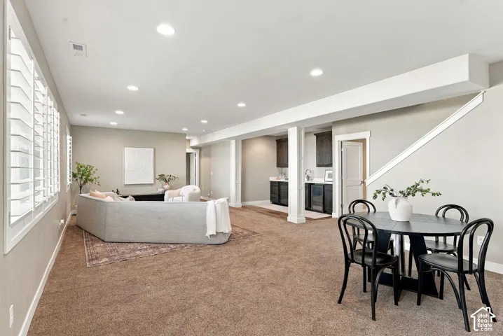 Spacious living area featuring neutral carpeting, recessed lighting, and a built-in wet bar with dark cabinetry