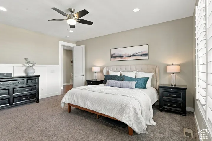 Main Floor primary bedroom, recessed lighting with a ceiling fan, plush carpeting, white paneling, and interior plantation shutters