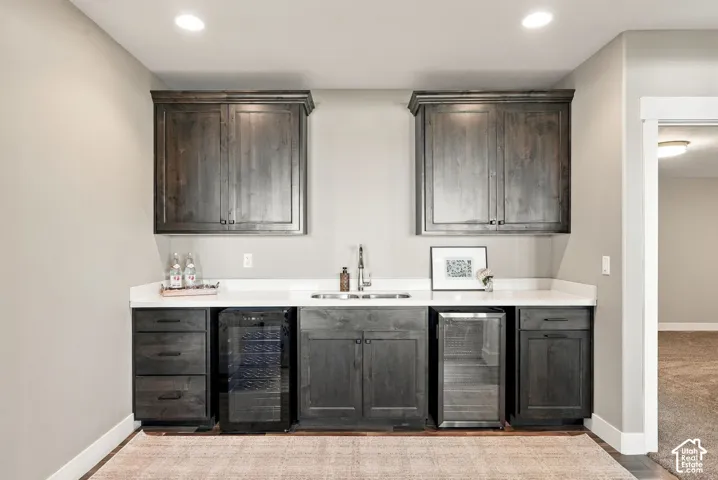 Basement built-in wet bar featuring dark wood-finish cabinetry, white countertops, dual beverage refrigerators, and a stainless steel sink with a gooseneck faucet