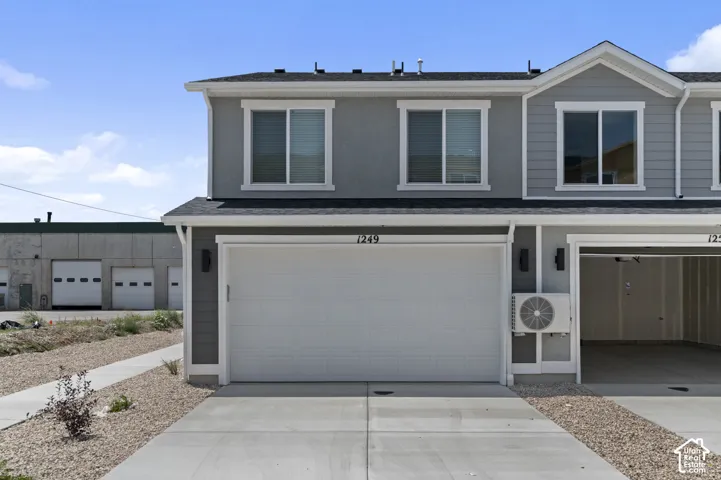 Modern two-story home featuring a spacious three-car garage with white paneled doors, clean concrete driveway, and contemporary gray exterior siding