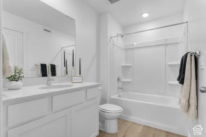 White vanity with an integrated sink and chrome faucet, full-width wall mirror, wood-finish flooring, and a white shower-over-tub unit