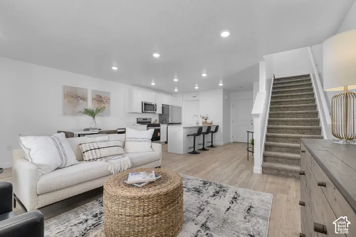 Open-concept living area featuring wood-finish flooring, recessed lighting, white cabinetry, and stainless steel appliances