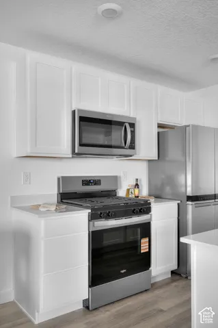 White shaker cabinetry, stainless steel appliances, light-toned countertops, and wood-finish flooring