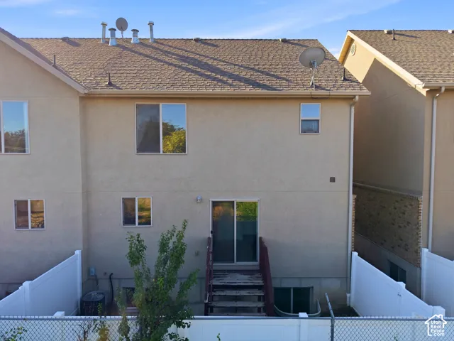 Rear exterior featuring a sliding glass door, multiple windows, and a private perimeter fence