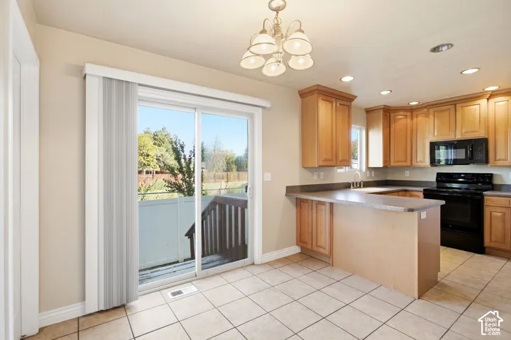 Kitchen with wood-finish cabinetry, black appliances, a peninsula island, and tile flooring