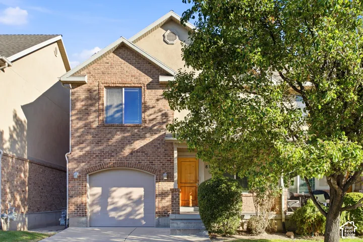 Charming brick home featuring a two-car garage with paneled doors, blue-trimmed window accents, and warm wood-finish entry door