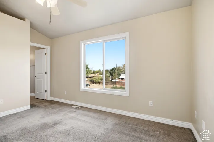 Carpeted room with a ceiling fan, a window with white trim, a white interior door, and light-colored walls