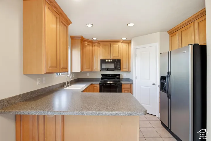 Kitchen featuring wood-finish cabinetry, speckled countertops, stainless steel refrigerator, black range, and recessed ceiling lighting