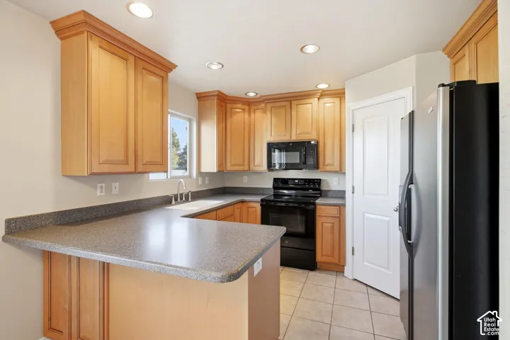 Kitchen featuring honey-toned wood cabinetry, U-shaped countertops, stainless steel refrigerator, black range, and recessed lighting