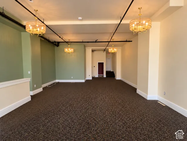 Recessed lighting, exposed conduit, decorative chandeliers, patterned carpeting, and white baseboards