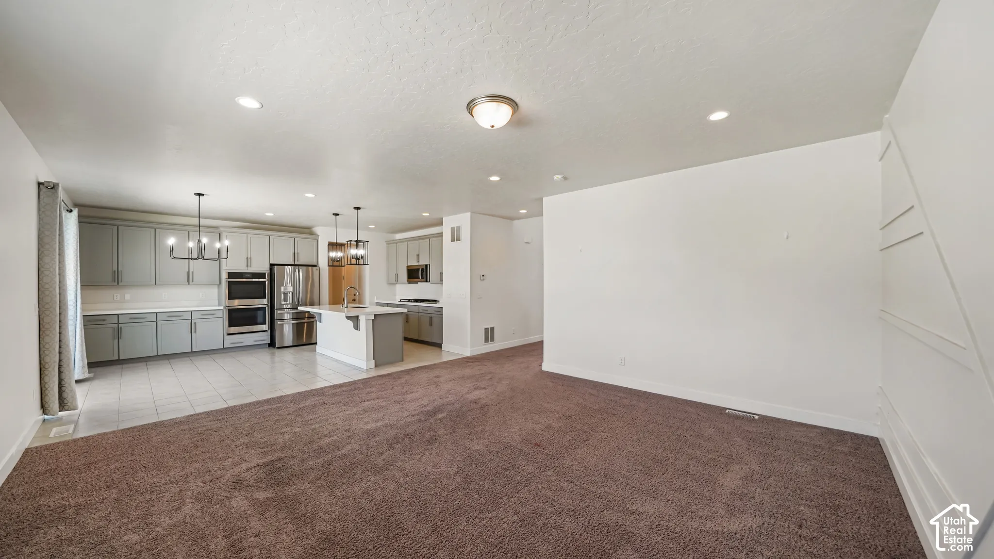 Open-concept living space with textured brown carpeting, recessed lighting, and a chandelier
