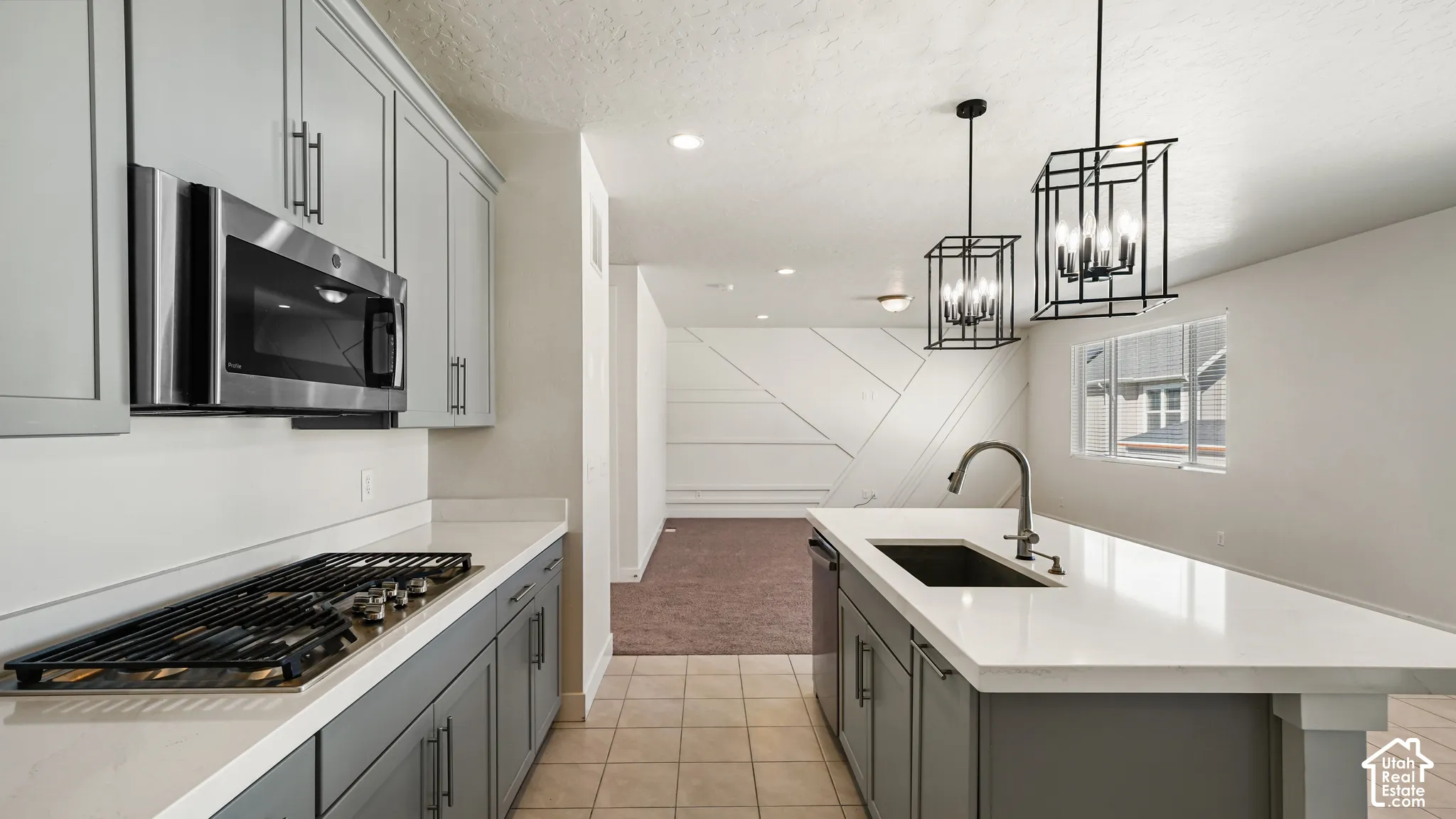 Kitchen featuring light gray cabinetry, stainless steel microwave, gas cooktop, and an island with a built-in sink and two pendant lights