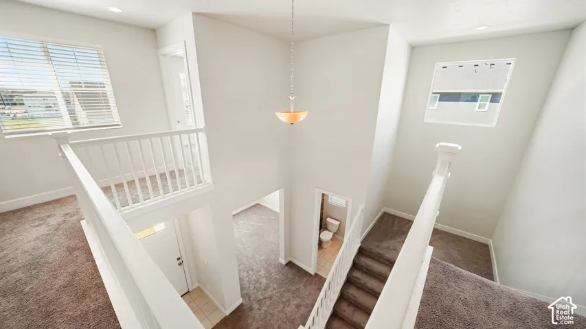 Open staircase with white railings and wood-finish treads, pendant lighting fixture, and neutral carpet flooring throughout the upper landing