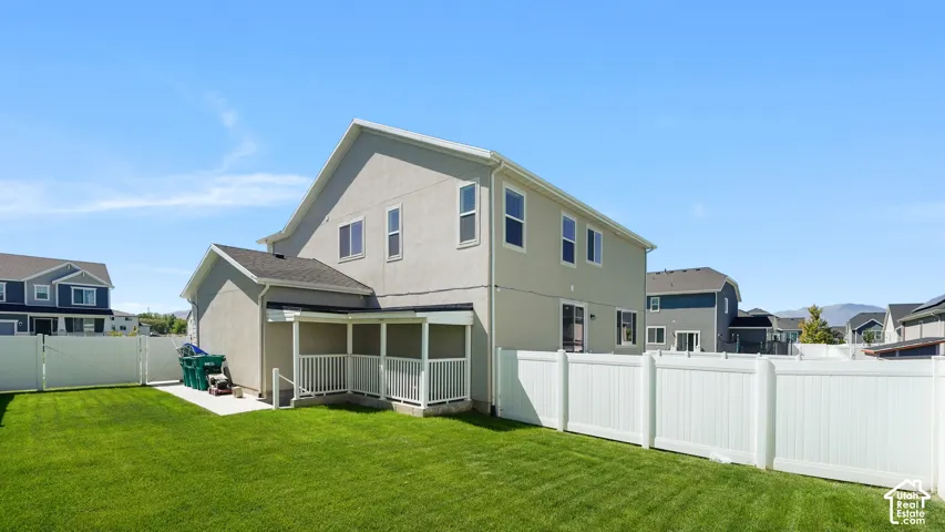 Expansive green lawn, white vinyl privacy fencing, two-story stucco exterior, covered patio, and multiple windows