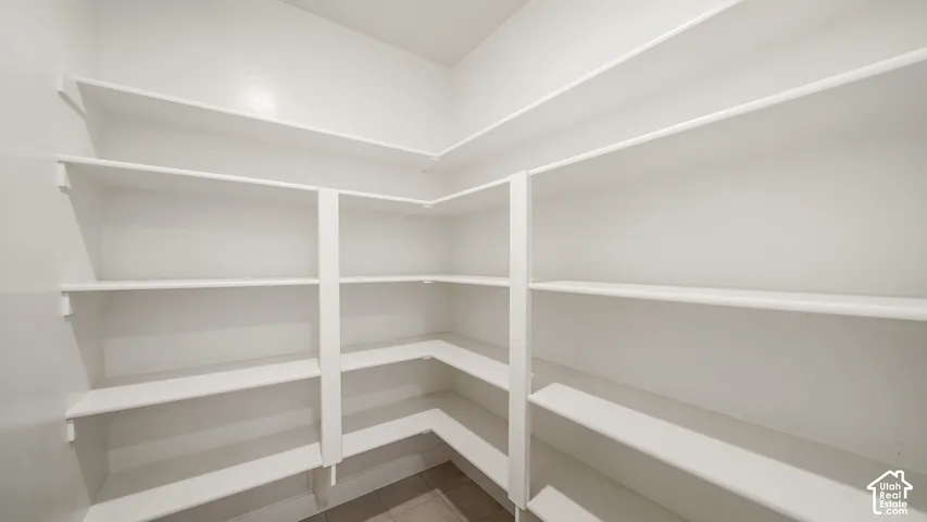 Corner pantry featuring extensive white shelving and tile flooring