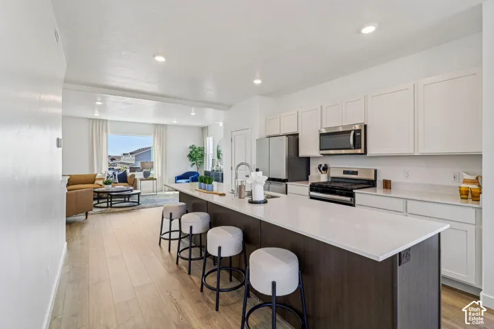 Kitchen featuring a spacious island with seating, white shaker cabinetry, stainless steel appliances, and wood-finish flooring