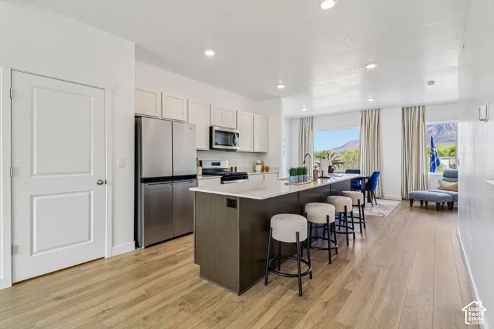 Open-concept living area with wood-finish flooring, a kitchen island with seating, stainless steel appliances, and recessed lighting