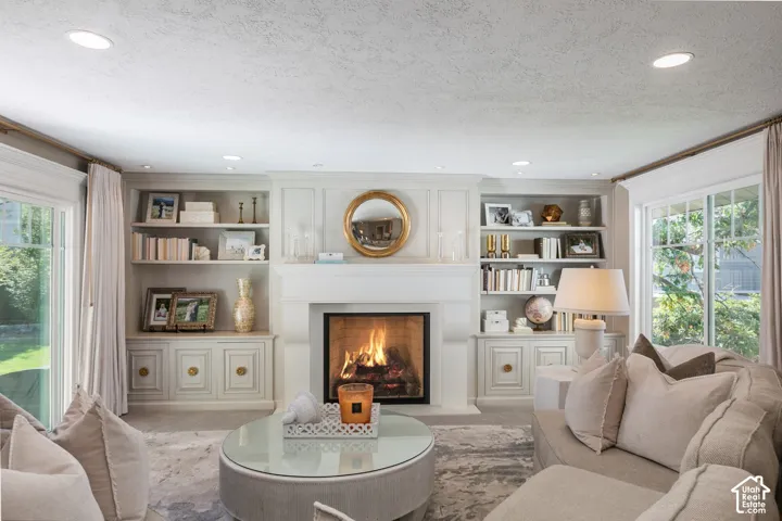 Built-in cabinetry with display shelving, a central fireplace, multiple recessed lights, and large windows with natural light