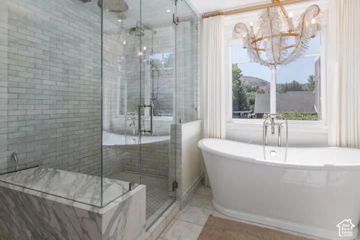 Freestanding soaking tub with floor-mounted faucet, walk-in shower with glass enclosure, subway tile shower walls, marble shower bench, and a decorative chandelier