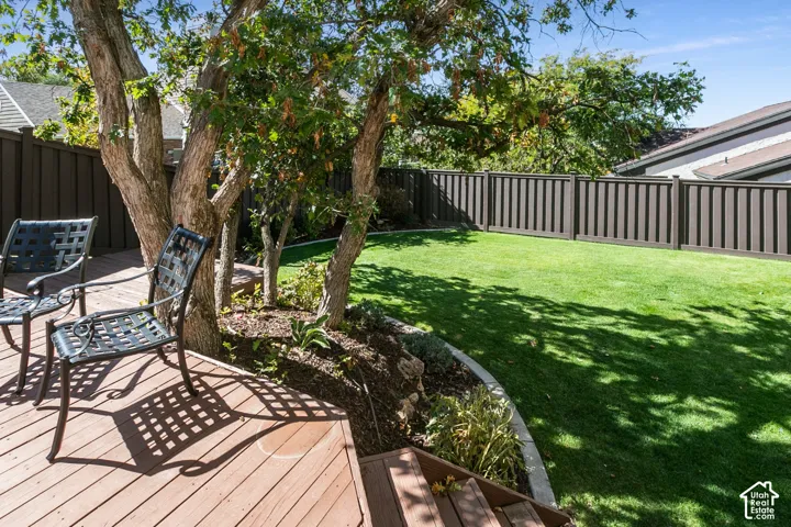 Expansive backyard oasis featuring mature shade trees, manicured lawn, composite deck with integrated seating areas, and professional-grade metal fencing