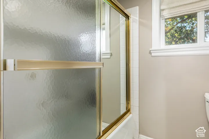 Frosted glass shower enclosure with brass-finish framing, white wall tile, and a single window with a privacy blind