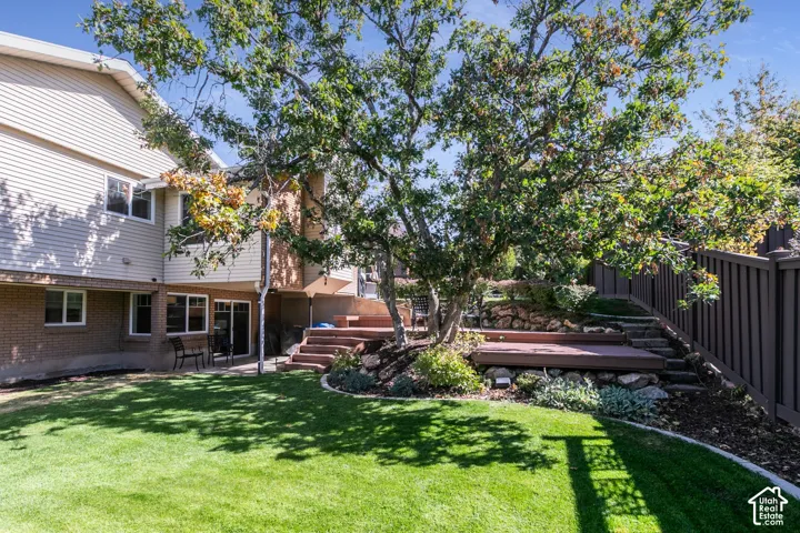 Expansive backyard featuring a manicured lawn, a large mature tree, multi-level composite decking, a retaining wall with integrated plantings, and a privacy fence
