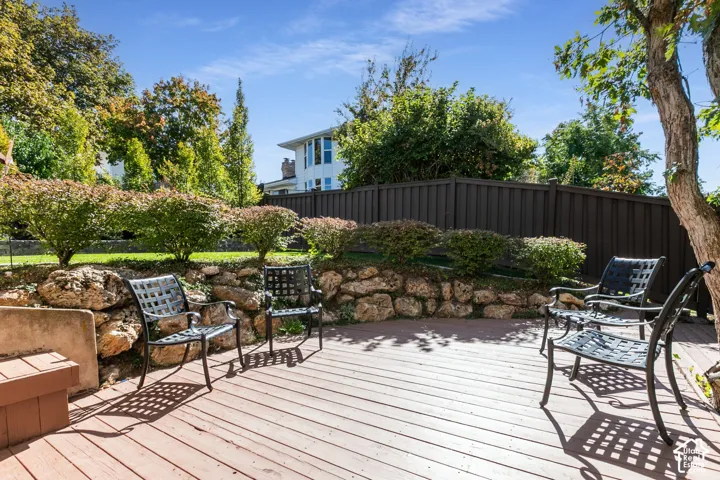 Wood-finish decking with a stone retaining wall, established landscaping, and a privacy fence