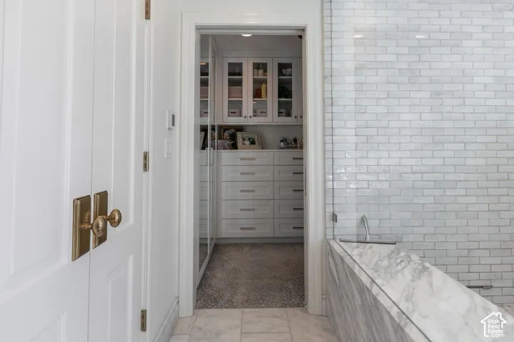 Spa-inspired primary bathroom featuring white subway tile walls, a freestanding soaking tub with marble surround, polished chrome fixtures, and tile flooring