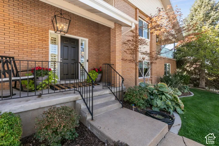 Brick exterior featuring a covered porch with a black wrought iron railing, concrete steps, a dark-paneled door with sidelights, and a prominent hanging lantern fixture