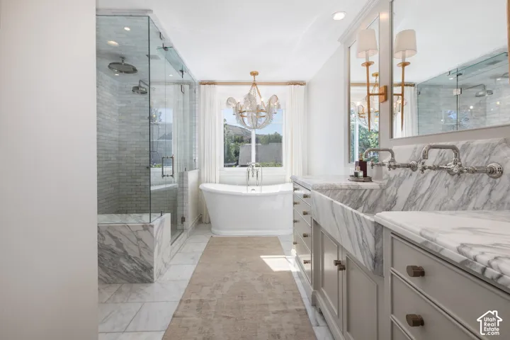 Freestanding soaking tub, large glass-enclosed shower with a bench, dual vanity with wall-mounted faucets, marble countertops, and light-toned cabinetry