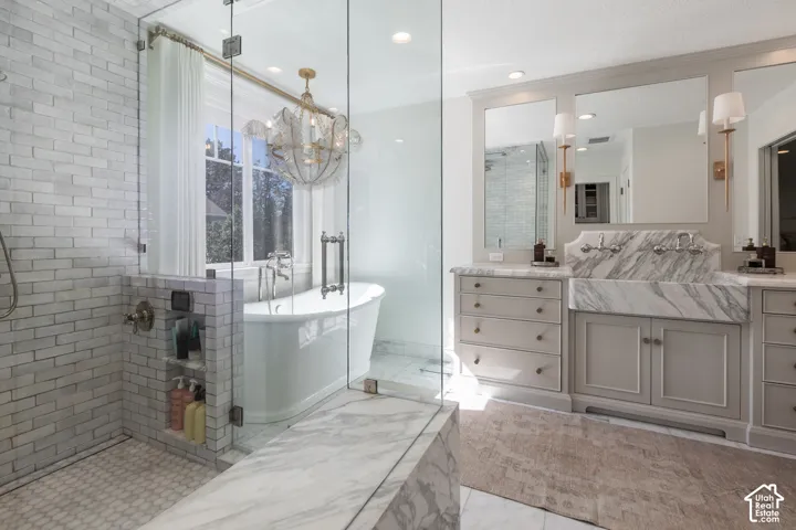 Glass-enclosed shower with subway tile and hexagon mosaic flooring, freestanding soaking tub, dual vanity with undermount sinks, wall-mounted faucets, and marble countertops
