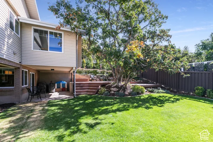 Expansive lawn with a terraced wood-finish deck, established tree, and privacy fencing