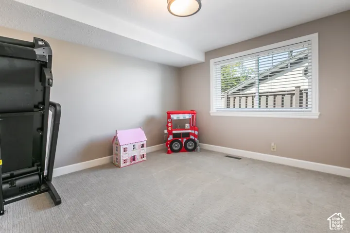 Recessed ceiling light fixture, neutral tone painted walls, light-colored carpet flooring, and a white-framed window with blinds