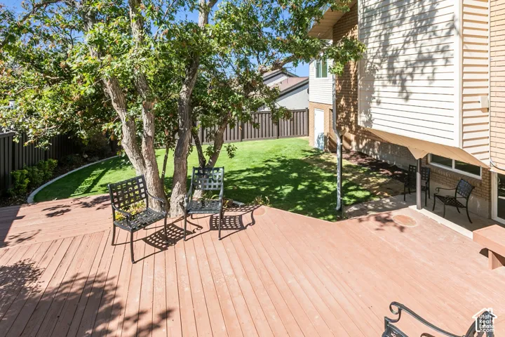 Expansive backyard featuring a large wood-finish deck, lush lawn, mature trees, and privacy fencing