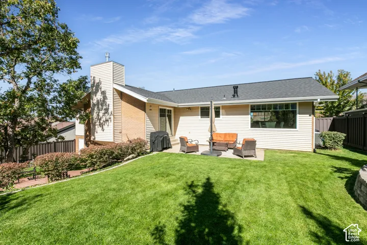 Expansive lawn with a concrete patio, a brick and siding exterior, a sliding glass door, and a retaining wall