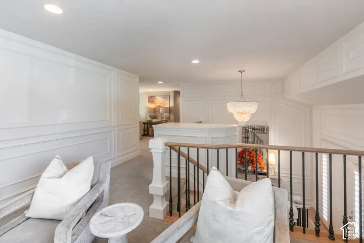 White paneled walls, recessed lighting, tiered chandelier, wooden handrail, and black iron balusters